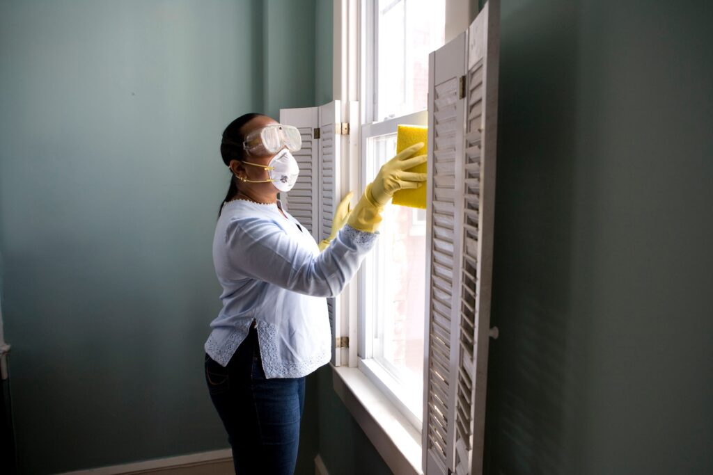 women in white shirt and denim pant cleaning window wearing yellow gloves