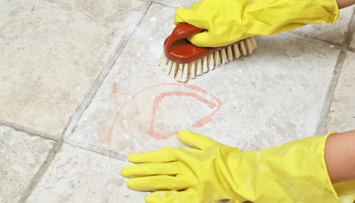 person cleaning tiles with a brush wearing a yellow gloves 